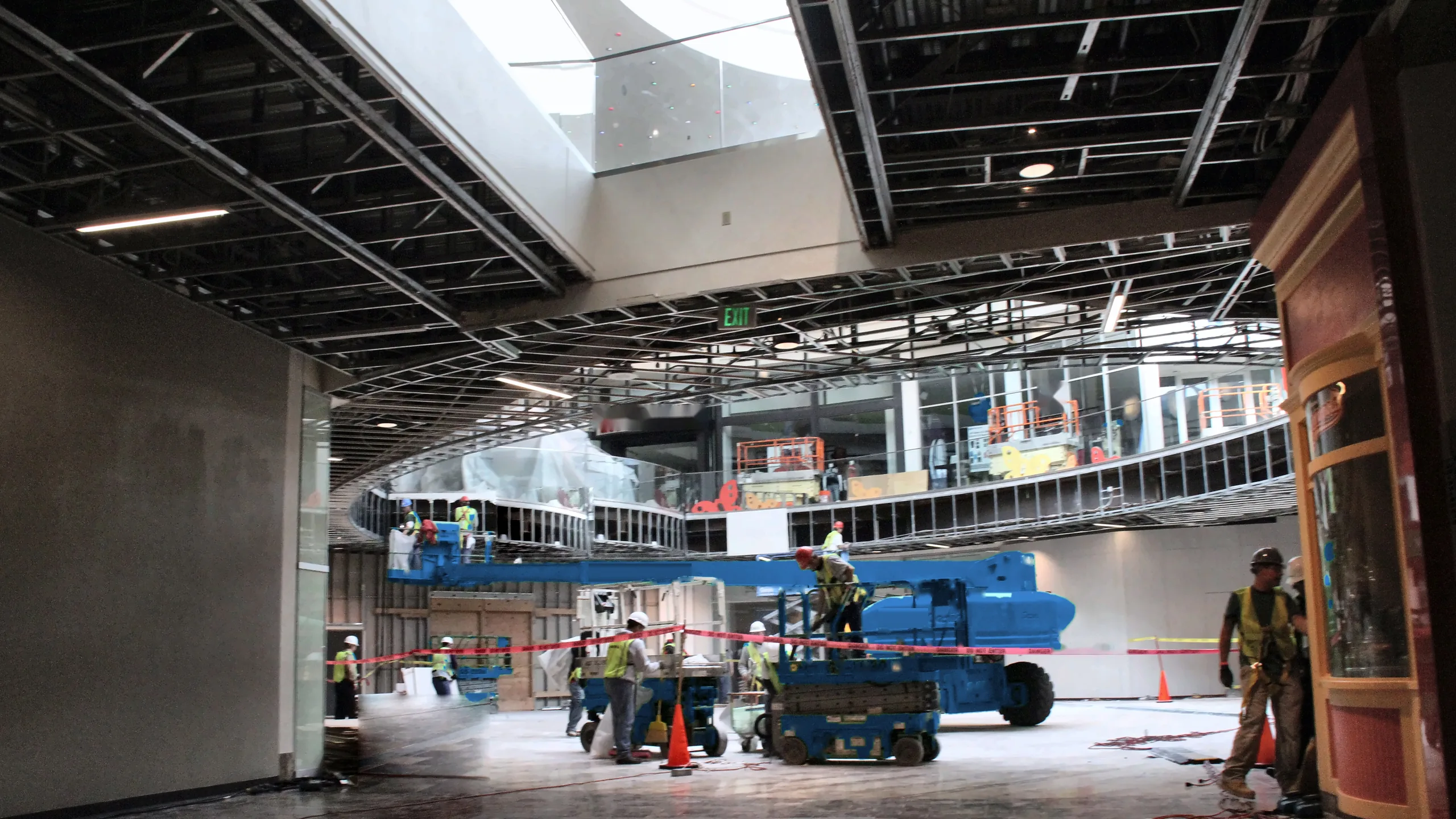 Crew renovating a two-story shopping center atrium with blue boom and scissor lifts under an open ceiling grid and skylight in Northern California
